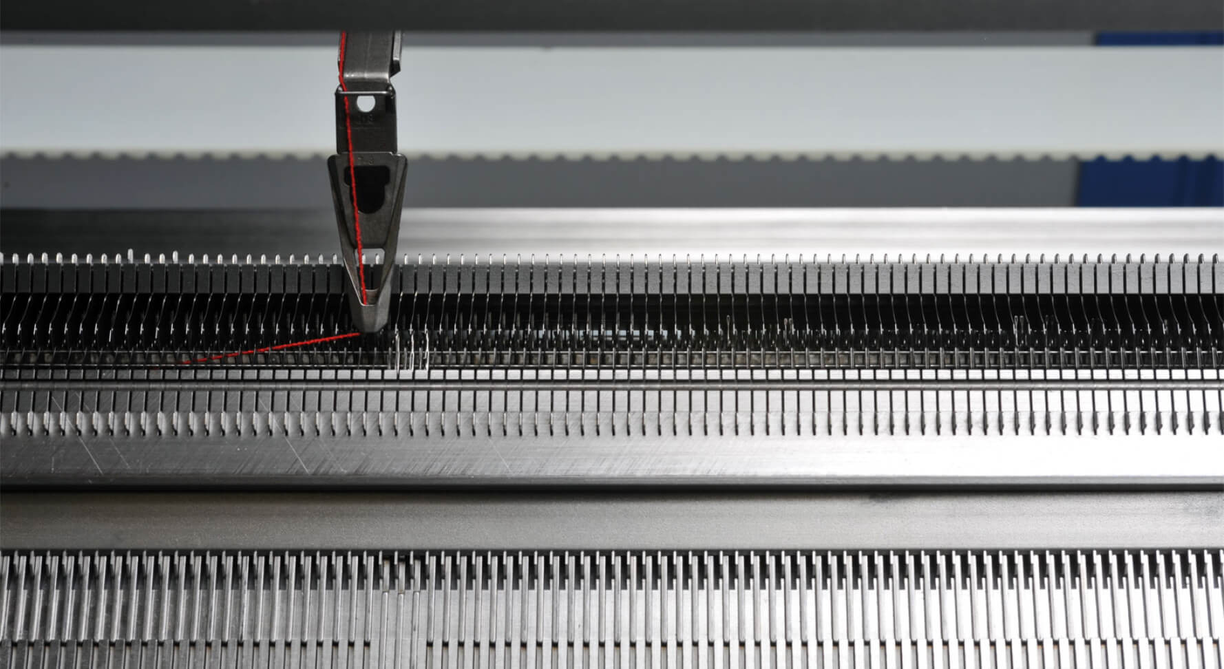 Flat knitting machine with yarn carrier. One read thread is being knitted.